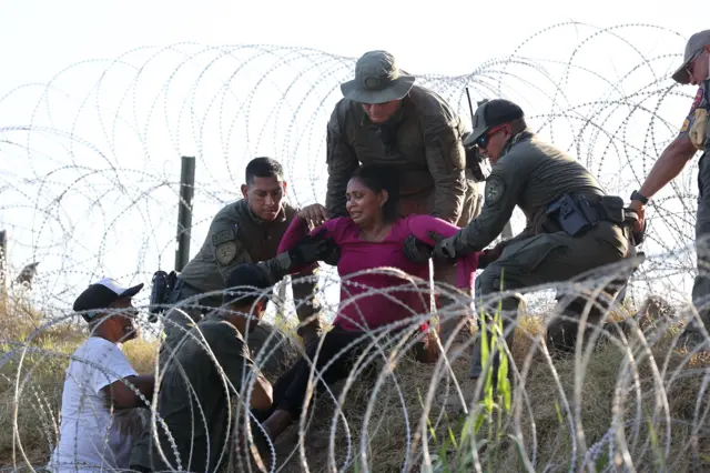 Policiais estaduais do Texas auxiliam migrantes passando pelo arame farpado ao longo do Rio Grande em Eagle Pass, no Texas, em 1º de agosto de 2023. Foto de ADAM DAVIS/EPA-EFE/REX/Shutterstock