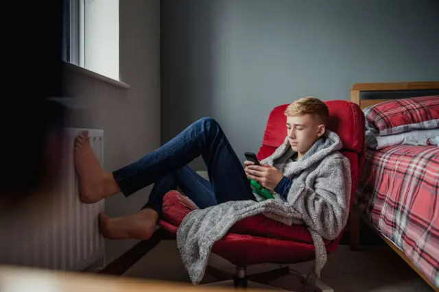 Garoto sentado em cadeira no quarto navegando no celular