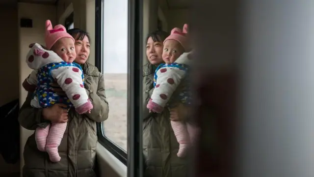 Uma mulher chinesa segura seu bebê nos braços próximo à janela de um trem