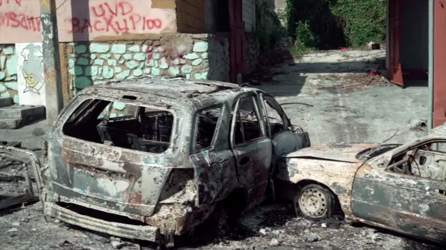 Dois carros queimados perto de um muro com pichações