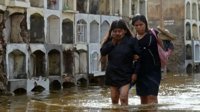 Duas mulheres caminham no Peru por uma área alagada pelas chuvas