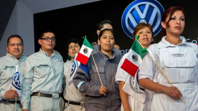 Trabalhadores da fábrica da Volkswagen em Puebla, no México, carregando a bandeira do país sob o logotipo da marca.