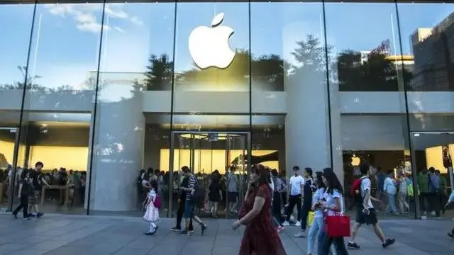 Foto da fachada de uma loja da Apple, com a maçã no topo, e pessoas passando na frente 