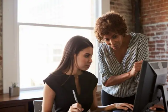 Duas mulheres trabalhando em frente a uma tela de computador