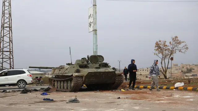 Pessoas passam por um tanque abandonado pelas tropas sírias depois que os combatentes da oposição assumiram o controle da cidade de Hama, na Síria, em 07 de dezembro de 2024. 