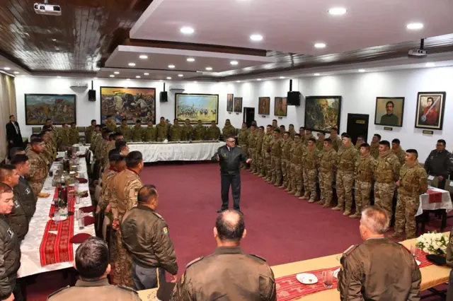 Em sala, Zúñiga aparece no centro falando, rodeado por fileiras de militares 