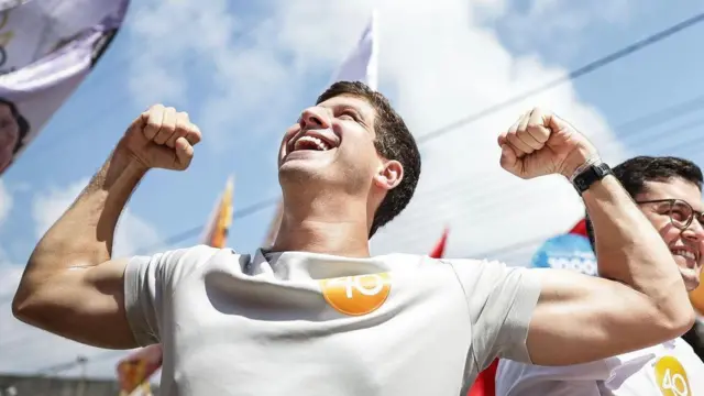 João Campos sorridente e com os graços dobrados para cima em demostração de força