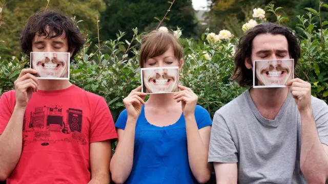 Dois homens e uma mulher segurando fotos de um sorriso em frente ao rosto