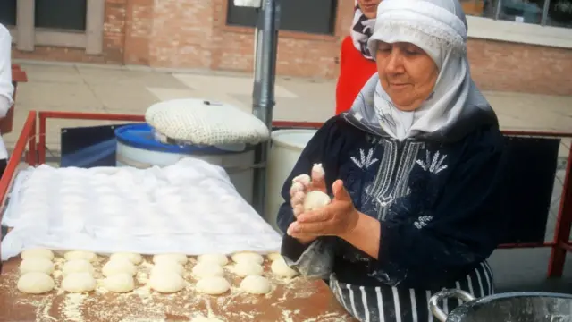 Mulher em barraquinha na rua preparando massa de prato típico