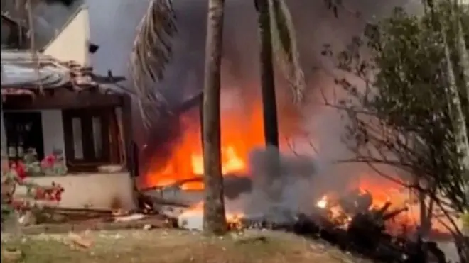 Imagem mostra uma casa ao lado esquerdo com muitas chamas e fogo ao redor, onde o avião caiu.