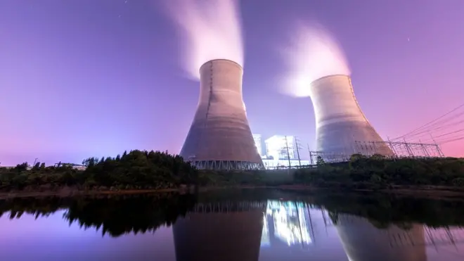 Imagem de chaminés de usina nuclear sob um céu de por-do-sol púrpura