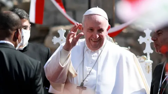 Pope Francis attending a prayer service in Mosul's Old City during a visit to Iraq in March 2021.  He is smiling and waving