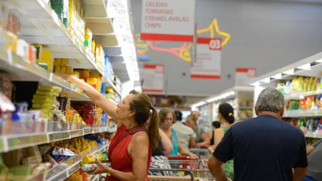 Mulher pega alimentos processados e ultraprocessados em prateleira