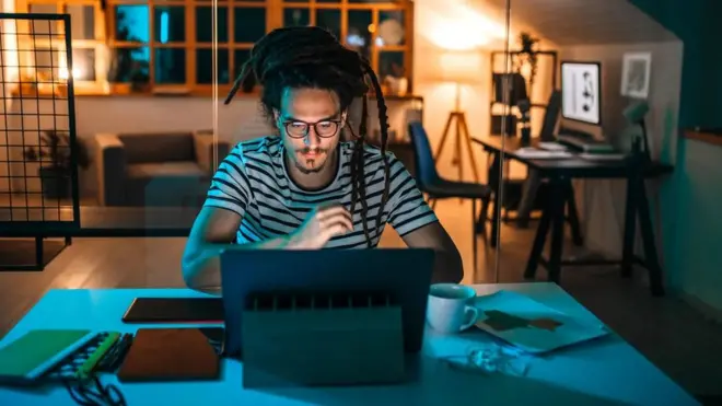 Homem olha computador em sala de casa