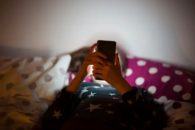 Criança deitada na cama com celular em frente ao rosto