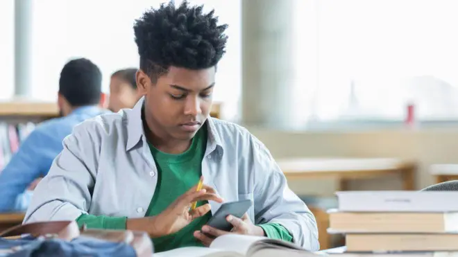 Adolescente mexendo em celular na sala de aula 