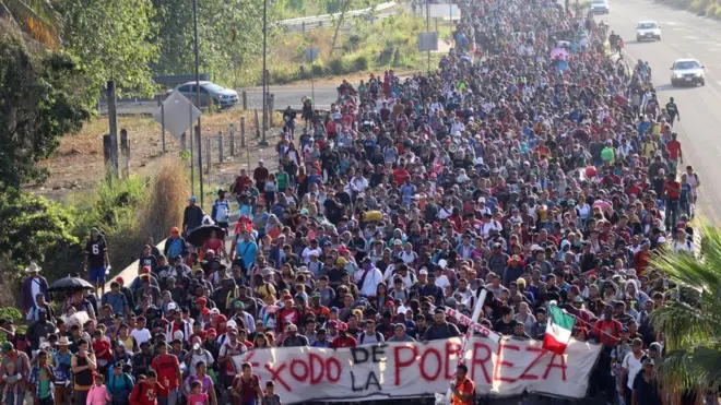 Grupo caminha com uma faixa que diz "Êxodo da Pobreza" em espanhol