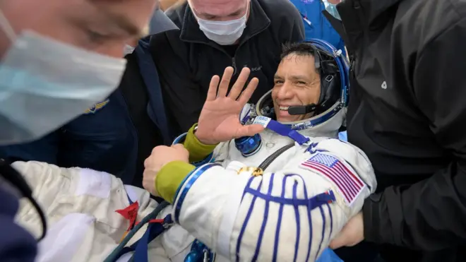 Frank Rubio, um homem de pele clara, em roupa de astronauta, sendo transportado por outras pessoas