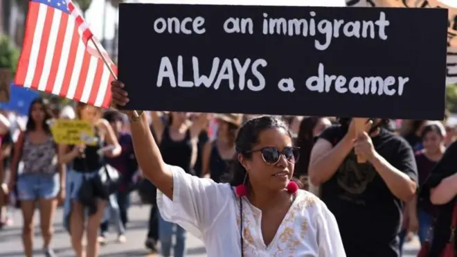 Mulher levanta bandeira dos EUA perto de cartaz que diz: 'Uma vez imigrante, sempre um sonhador'