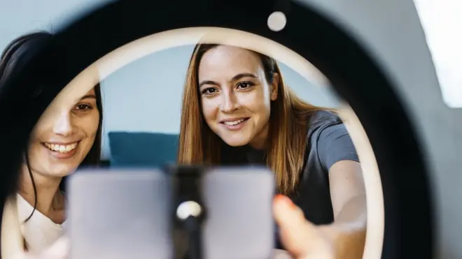 Two young women film themselves on their mobile phones