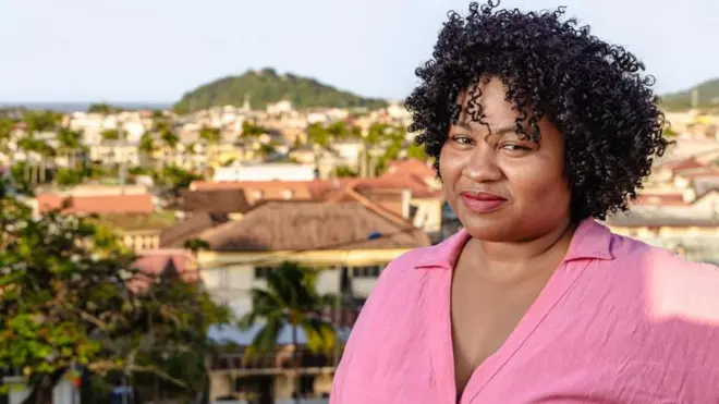 Imagem de uma mulher negra, blusa rosa, com cidade ao fundo