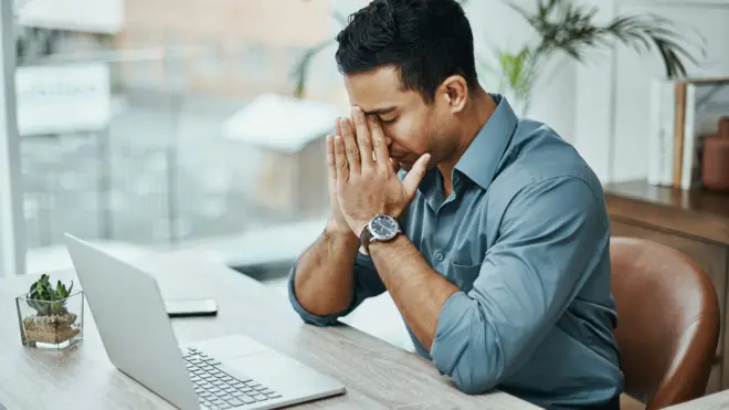 Homem com a mão no rosto preocupado em frente a laptop