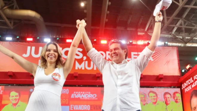 Prefeito de Fortaleza, Evandro Leitão, comemorando vitória, com as mãos para o alto com mulher loira. Ambos sorriem