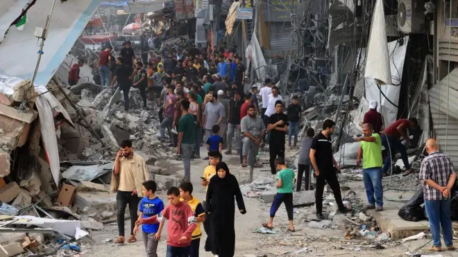 Palestinos caminham entre os escombros de edifícios destruídos e danificados no centro da cidade fortemente bombardeada de Khan Yunis, no sul da Faixa de Gaza, após bombardeio israelense durante a noite, em 10 de outubro de 2023