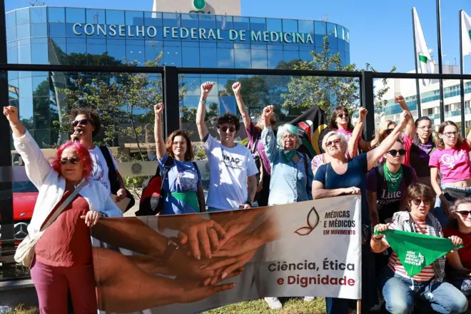 Mulheres protestando com cartazes em frente a prédio do CFM