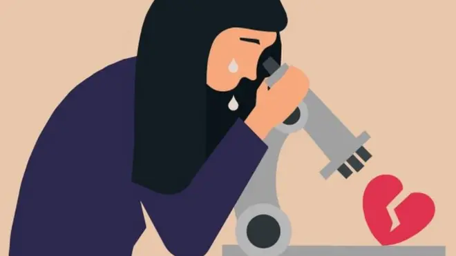 A woman looks at a broken heart through a microscope