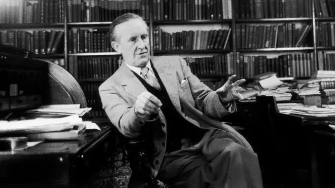 Tolkien sentado, conversando, com prateleiras de livros ao fundo