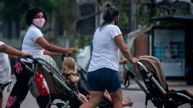 Três babás de camisa branca empurrando carrinho na rua