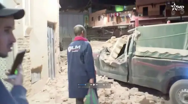 Veículos rodeado de destroços; dois homens em pé estão ao lado dele