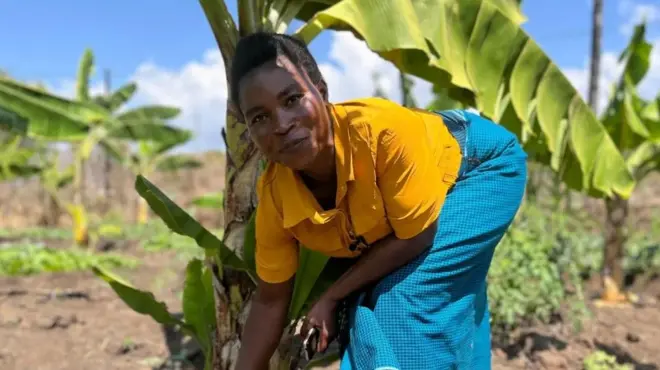 Une femme souriante et accroupie à côté d'un bananier