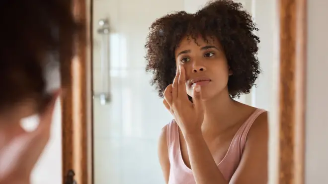 Mulher passando cosmético em frente a um espelho