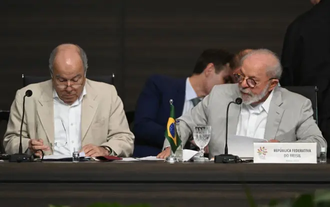 Mauro Vieira e Lula sentados diante de mesa em evento; Lula fala ao microfone