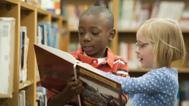 Garoto negro e garota branca em biblioteca