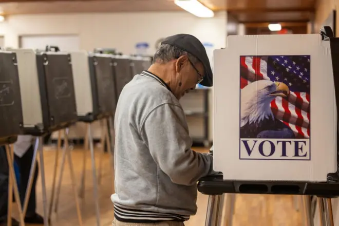 Homem deposita voto em um local de votação antecipada na Carolina do Norte na imagem, aparece a urna com o símbolo de votação, onde está escrito "vote" e a foto de uma águia com a bandeira dos EUA