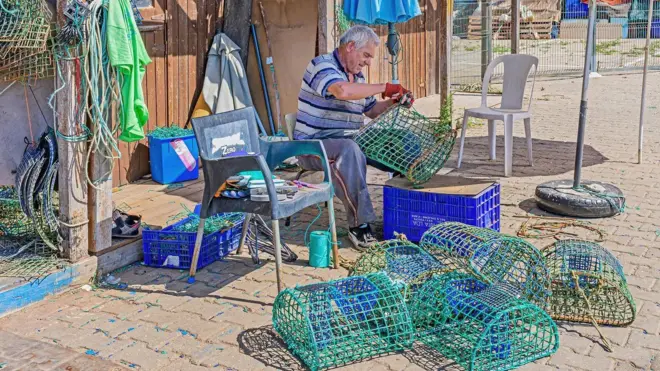 Pescador remendando armadilha para polvos no Algarve, em Portugal