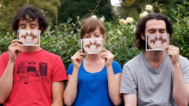 Dois homens e uma mulher segurando fotos de um sorriso em frente ao rosto