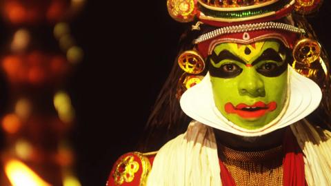 Inel wearing green face paint and expressive eye make up is dressed for a Kathakali drama.