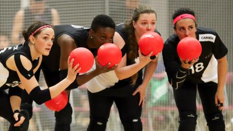 Girls holding dodgeballs discussing tactics on the dodgeball court.