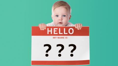 Baby holding up name badge with question marks on it.