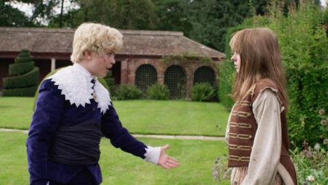 Dodger's usual dark hair is dyed blonde and curled, he talks to Polly in a nice looking garden.