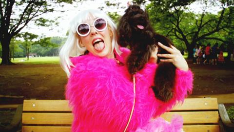 A woman dressed in pink sits on a park bench and holds up a dog.