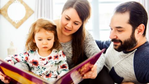 Parents are reading a book with their young daughter.