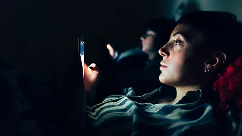 A woman uses a smartphone in bed (Credit: Getty Images)