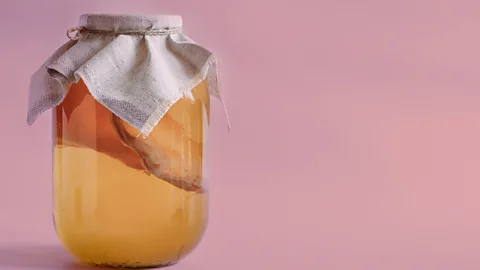 A jar of kombucha against a pastel pink background (Credit: Getty Images)