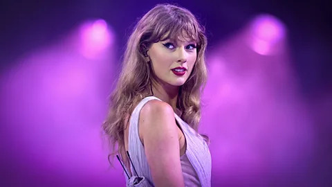 Taylor Swift on the Eras tour with her back to the camera making heart shape (Credit: Getty Images)