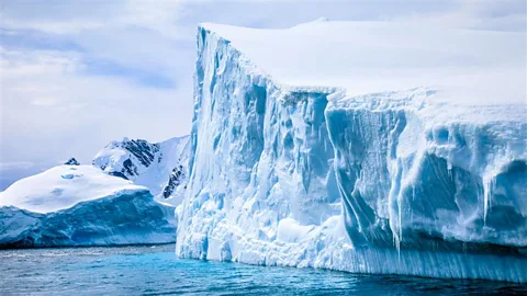 An enormous iceberg towers over some nearby land in Antarctica (Credit: Getty Images)